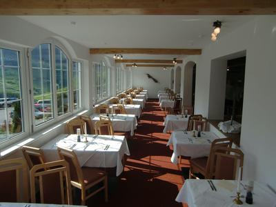 Hell beleuchteter Speisesaal mit weißen Tischdecken und Holzmöbeln neben Panoramafenstern.