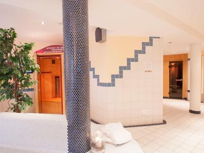 Moderner Wellnessbereich mit Sauna, weißen Fliesen, Säulen und grüner Zimmerpflanze.