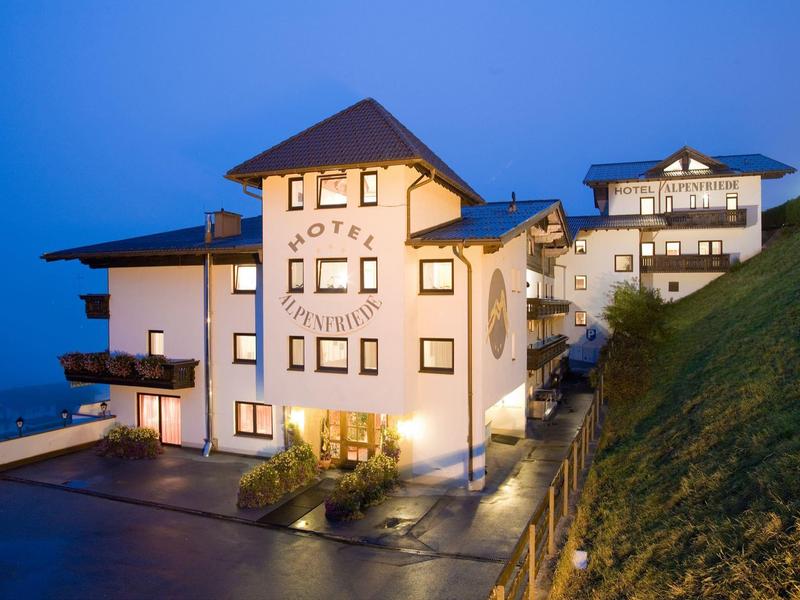 Weißes Berghotel mit braunem Dach am Hang bei Dämmerung, beleuchtet und ruhig gelegen.