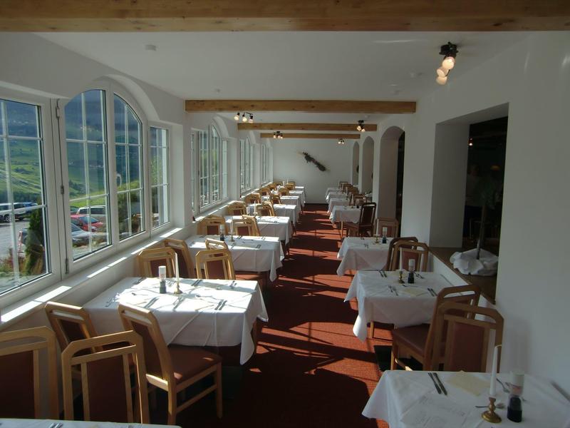 Hell eingerichtetes Restaurant mit großen Fenstern, Holzbalken und rot-weißem Boden.