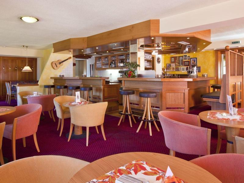 Gemütliche Bar mit runden Tischen, Stühlen und Theke in warmen Farben und rotem Teppich.