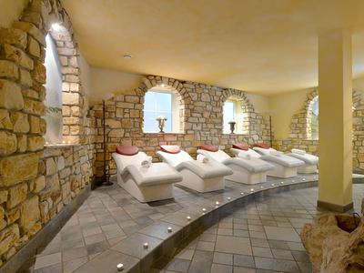 Ruheraum mit weißen Liegen, Natursteinwänden und weichem warmem Licht.