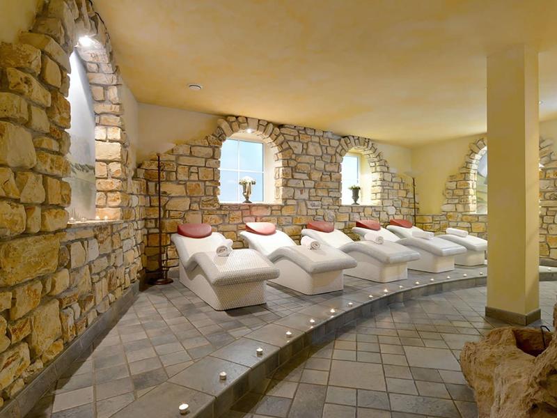 Ruheraum mit weißen Liegen, Natursteinwänden und weichem warmem Licht.