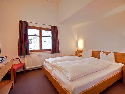 Ein einfach eingerichtetes Schlafzimmer mit Doppelbett, Schreibtisch, Stuhl und Fenster mit Vorhängen.