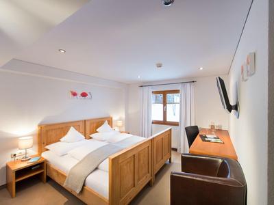 Hell eingerichtetes Schlafzimmer mit Holzmöbeln, großem Bett, Schreibtisch und Fernseher an der Wand.