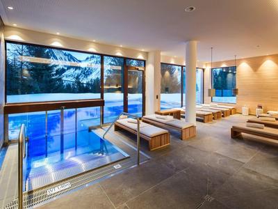 Moderner SPA-Bereich mit Innenschwimmbecken, Liegen und großer Fensterfront mit Außenblick.