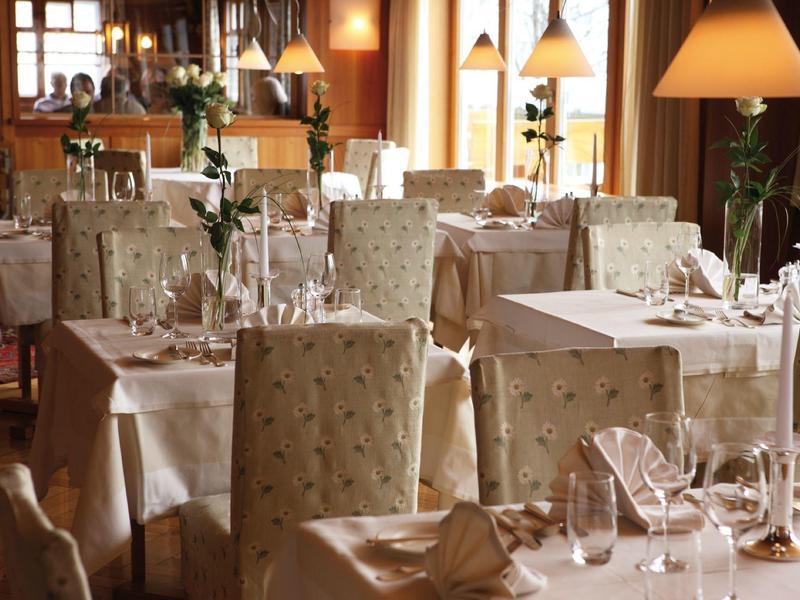 Elegantes Restaurant mit weißen Tischdecken, gepolsterten Stühlen und warmem Lampenlicht.