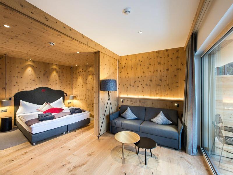 Modernes Hotelzimmer mit Holzdekor, Doppelbett, Sofa, Stehlampe und großem Fenster mit Balkonzugang.