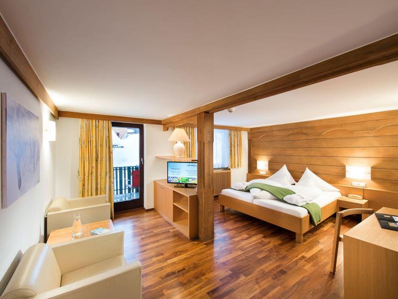 Helles Hotelzimmer mit Holzboden, Doppelbett, Sitzecke, Balkon und moderner Beleuchtung.