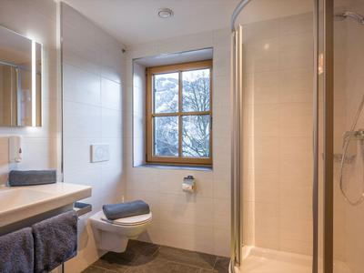 Jasna łazienka z prysznicem, toaletą, umywalką i oknem z widokiem na zewnątrz.