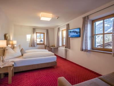 Jasny pokój hotelowy z dwoma łóżkami pojedynczymi, czerwonym dywanem i oknami z widokiem na góry.