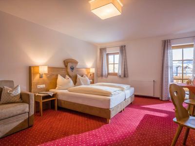 Světý hotelový pokoj s manželskou postelí, křesly, dřevěným nábytkem a kobercem.