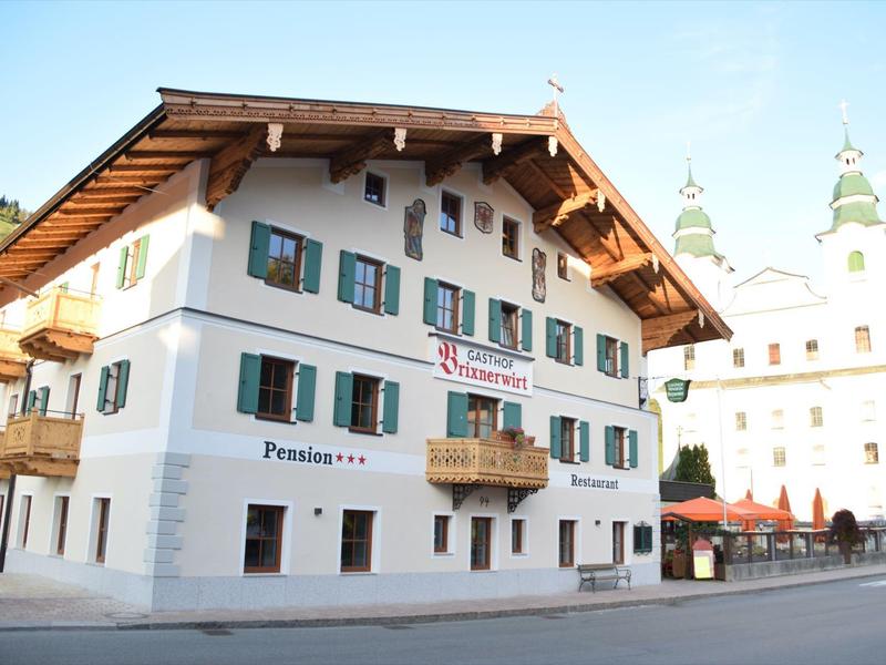 Bílá vícepatrová budova se zelenými okenicemi v tiché ulici.