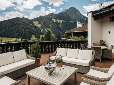Cozy terrace with seating furniture overlooking forested mountains under a clear sky.