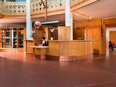 A bright hotel reception area with a wooden counter and a staff member behind the desk.