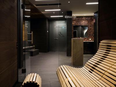 Moderne Saunalounge mit geschwungenen Holzbänken, dunklen Wänden und indirekter Beleuchtung.