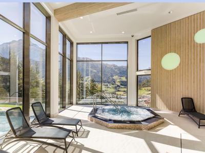 Moderner Wellnessbereich mit Hot Tub, Liegestühlen und großen Panoramafenstern mit Bergblick.