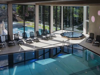 Modern indoor pool with large windows, lounge chairs, and view of outdoor pool area