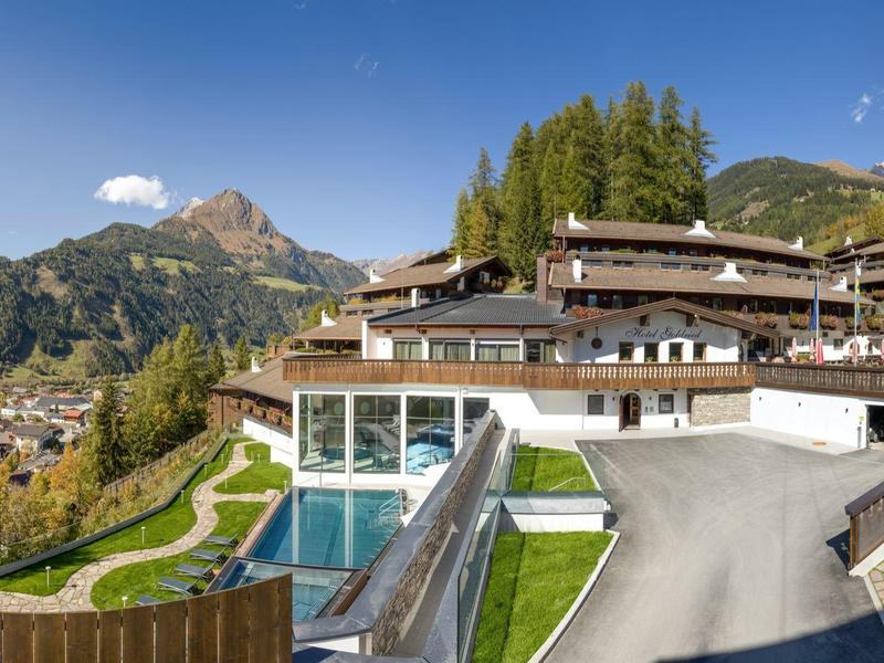 Bergdorf mit traditionellen Holzhäusern, grünen Wiesen und steinigen Wegen unter blauem Himmel.