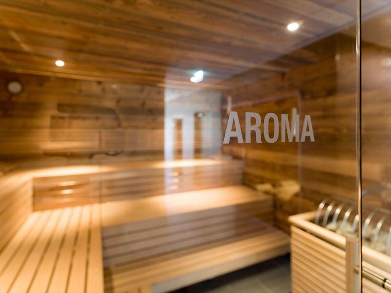 Holzsauna mit gestuften Bänken und Saunaofen, warme Beleuchtung, Glaswand mit Aufschrift "AROMA".