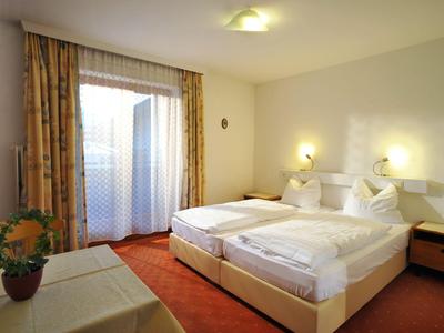 Licht ingericht hotelkamer met twee eenpersoonsbedden, tafel, bloem en groot raam met gordijnen.