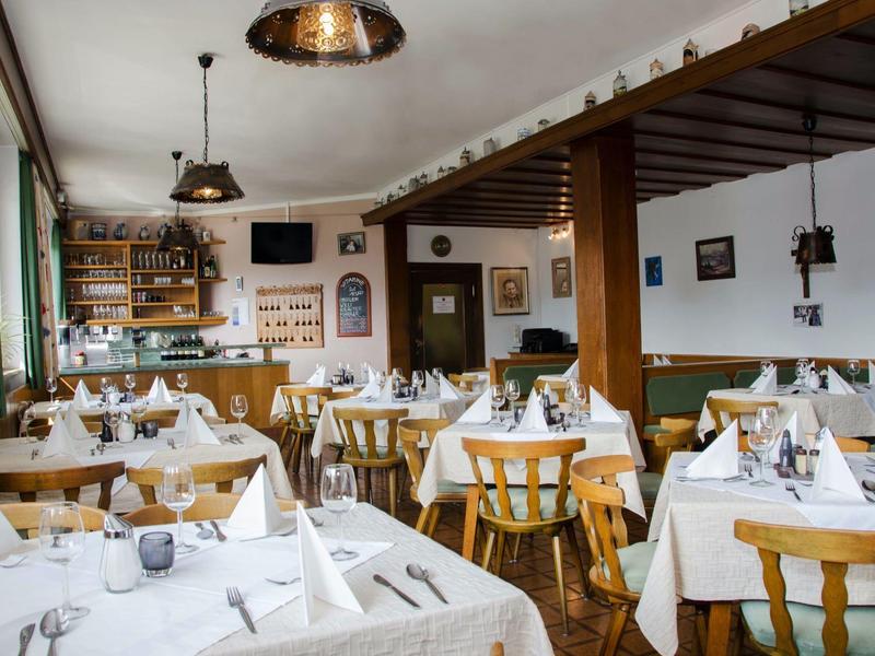 Hell eingerichteter Gastraum mit gedeckten Tischen, Holzstühlen und großer Fensterfront.