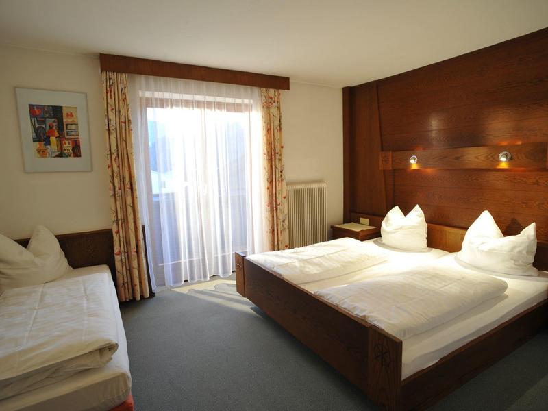 Hell eingerichtetes Schlafzimmer mit Doppelbett, Einzelbett, Vorhang und Balkonfenster.