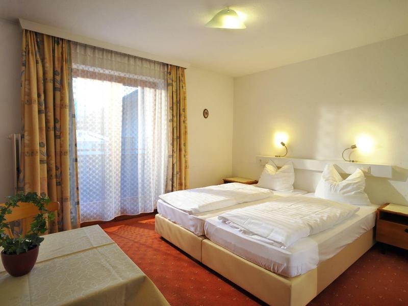 Gemütliches Schlafzimmer mit Doppelbett, zwei Nachttischen, Vorhängen und einem Blumentopf auf Tisch.