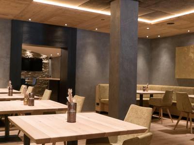 Nowoczesna jadalnia z jasnymi drewnianymi stołami i beżowymi krzesłami pod ciepłym oświetleniem.