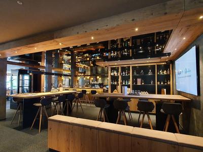 Nowoczesny bar hotelowy z drewnianymi meblami i półkami pełnymi butelek pod ciepłym oświetleniem.