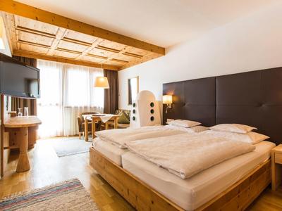 Bright hotel room with wooden furniture, a large bed, TV, and desk by the window.
