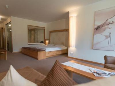 Spacious hotel room with a large bed, armchair, wooden furniture, and modern decor.