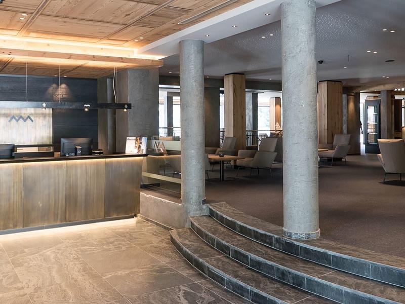 Modern hotel lobby with wooden reception desk, stone columns, and tiled floor.
