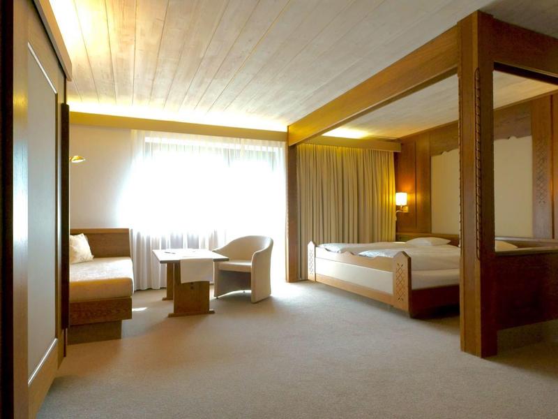 Spacious hotel room with bed, seating area, desk, and warm wooden accents.