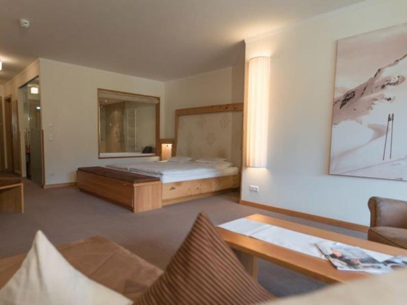 Spacious hotel room with a large bed, armchair, wooden furniture, and modern decor.