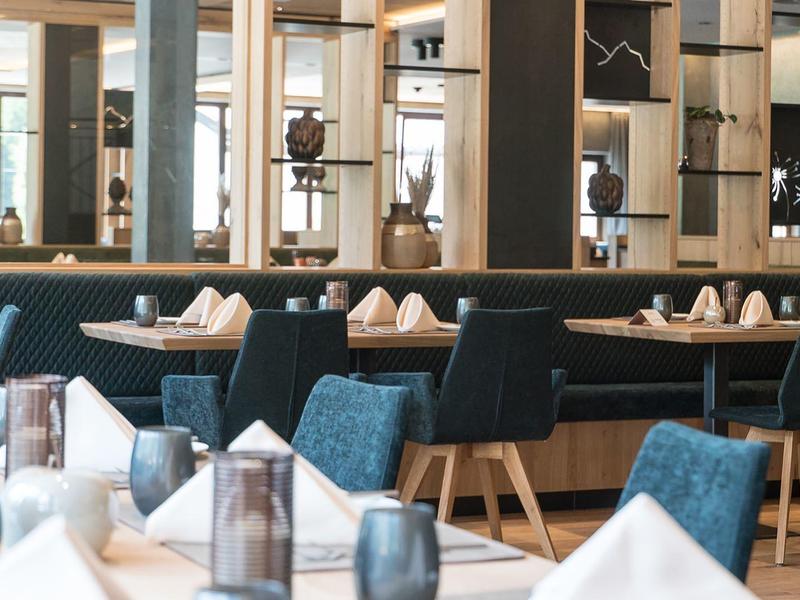 Modern hotel dining area with blue chairs, wooden tables, glassware, and decorative shelves.