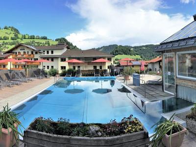 Großer Außenpool mit Liegestühlen und Gebäuden in einer ländlichen Umgebung unter blauem Himmel.