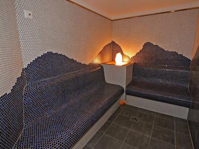 Salle de sauna avec carrelage mosaïque foncé et éclairage indirect dans le coin.
