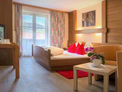 Chambre d'hôtel confortable avec lit, canapé, bureau et fenêtre de balcon en plein jour.