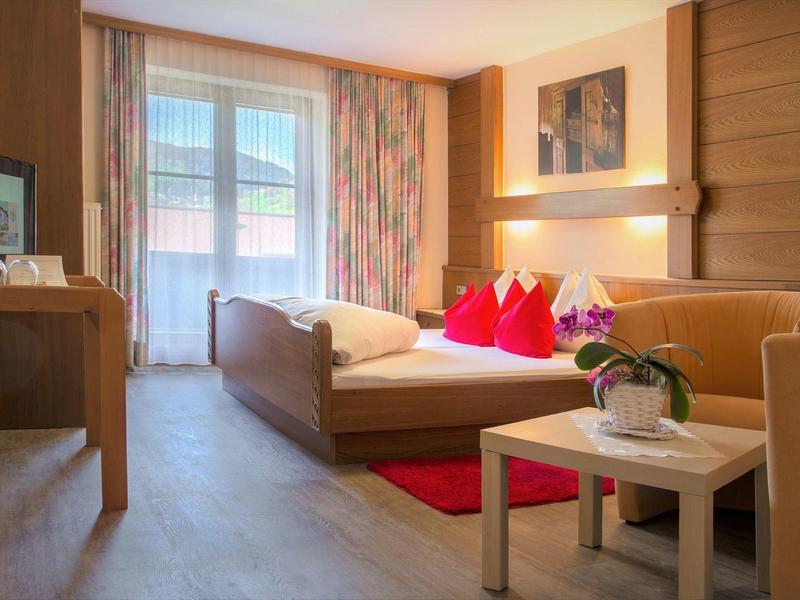 Chambre d'hôtel confortable avec lit, canapé, bureau et fenêtre de balcon en plein jour.