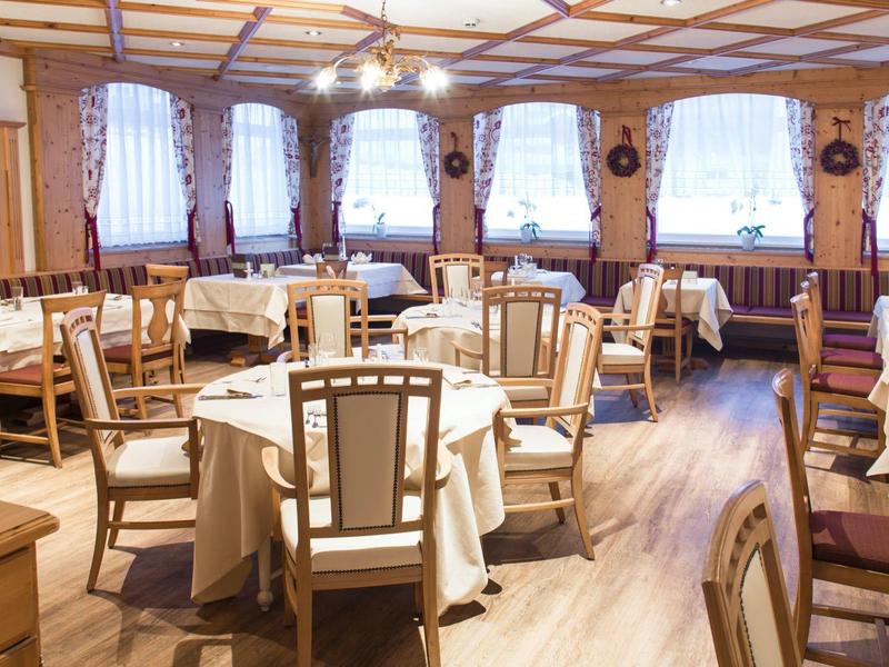 Heller, gemütlicher Speiseraum mit runden Tischen, weißen Tischdecken und Holzstühlen.