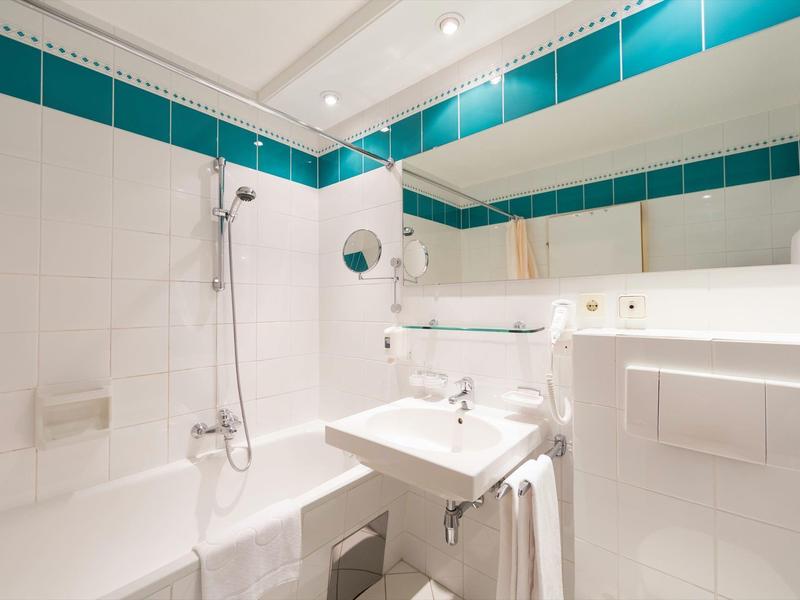 Helles Badezimmer mit weißer Badewanne, Waschbecken, großem Spiegel und türkisfarbenen Fliesen.