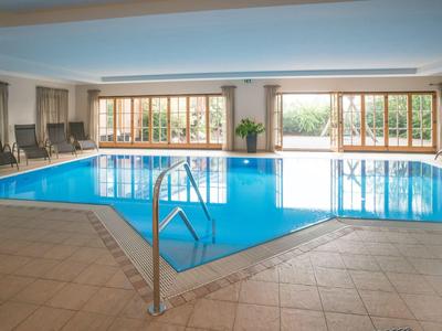 Piscina coperta con acqua azzurra, lettini e grandi finestre che danno sull'esterno.