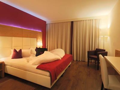 Camera d'hotel moderna con letto matrimoniale, scrivania, TV e illuminazione indiretta.