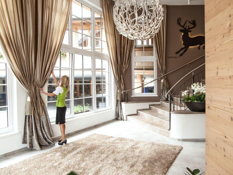 Jasná hotelová hala s velkými okny, závěsy a moderním kulatým stropním svítidlem.