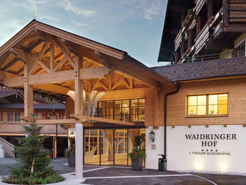 Vstup do tradičního alpského hotelu s dřevěnou architekturou a osvětlenými okny za soumraku.