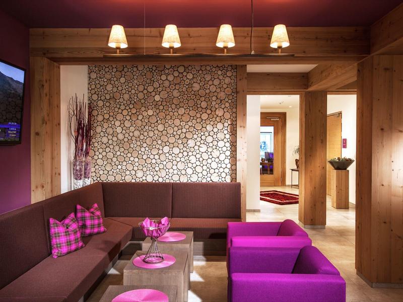 Pohodlná hotelová lounge s hnědým posezením, fialovými křesly a moderním osvětlením.