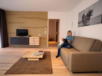 Cozy living room with sofa, TV, rug, and person reading a book.