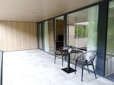 Modern balcony with table and two chairs next to large sliding glass doors.