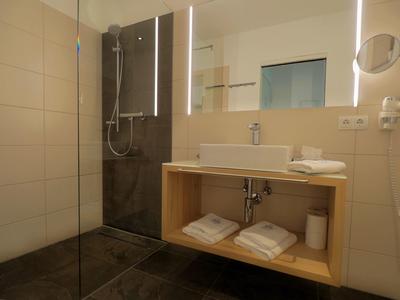 Modern hotel bathroom with walk-in shower, illuminated mirror, and wooden furniture.